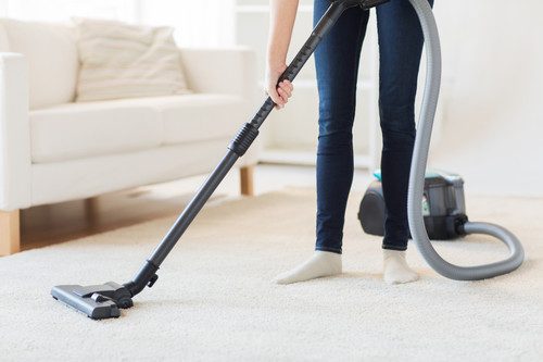 people, housework and housekeeping concept - close up of woman with legs vacuum cleaner cleaning carpet at home