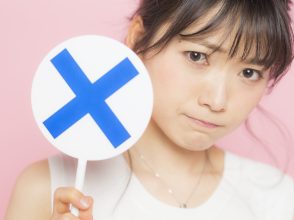 バツの札を上げる女性