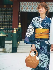上品なネイビーと爽やかブルーの色合わせが特徴的な、大花柄の浴衣。帯はオレンジ、手には大き目のかごバッグを持っている。