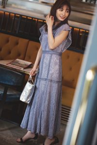 総レースの淡いブルーのワンピース。手にはシルバーのバッグ、足には黒のサンダルを身につけている。